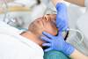 Professional beautician rejuvenating male face.
